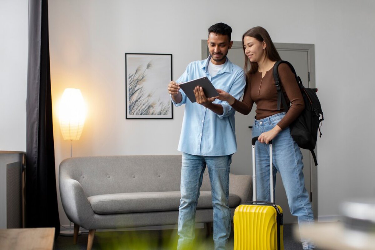 A man and a woman with a suitcase looking at a tablet in a modern living room.