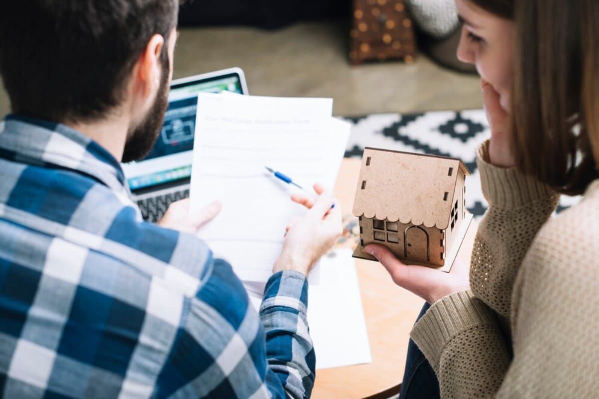Two people reviewing a mortgage application form with a laptop and a small model house on a table.