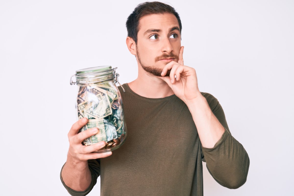 Man holding a jar full of money, looking thoughtful.