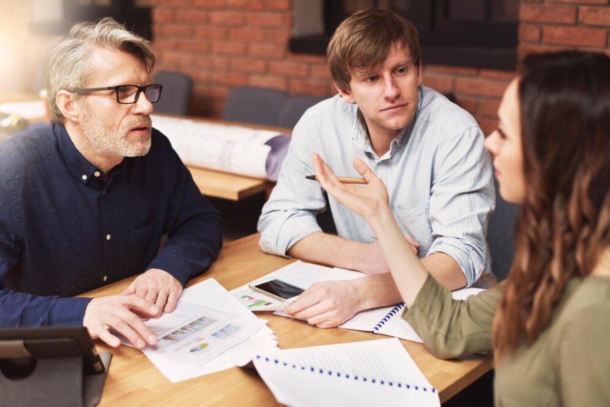 Three professionals discussing documents at a table in a well-lit office space.