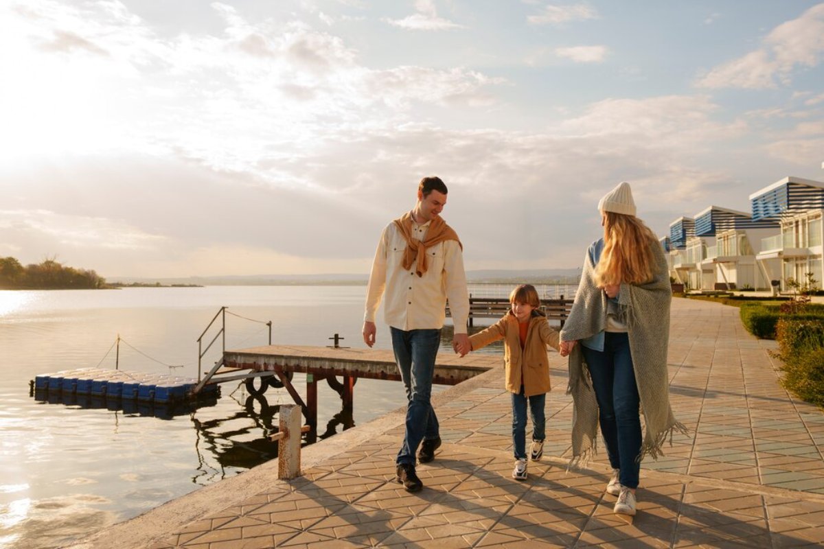 A family walks hand in hand on a lakefront promenade during a sunny morning.