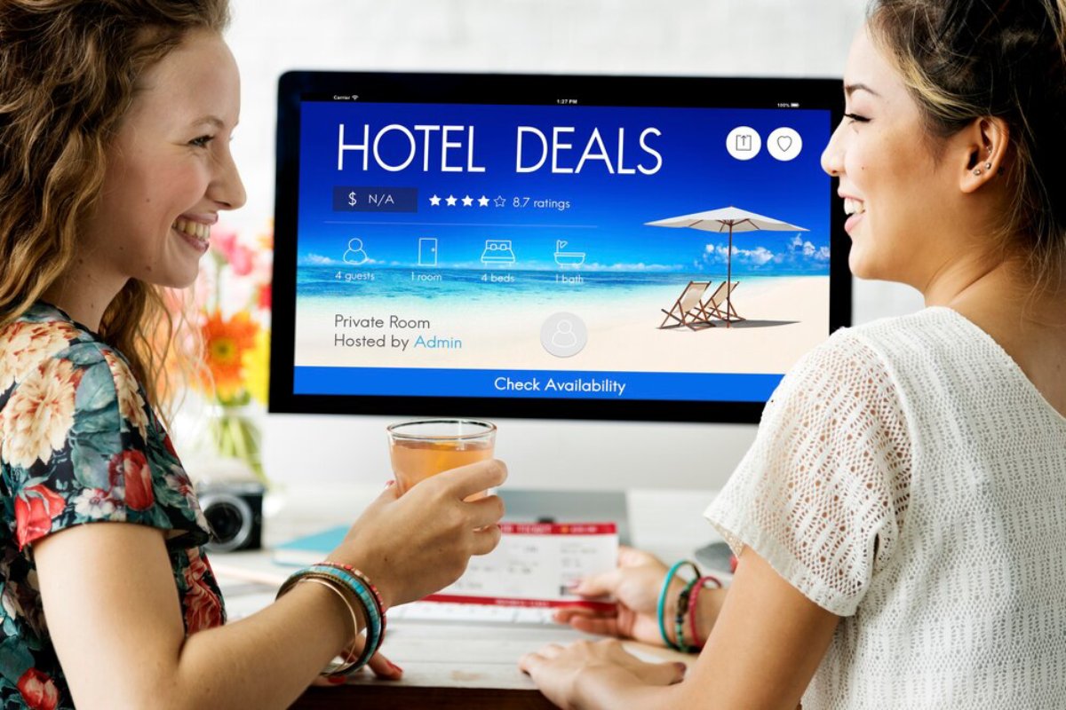 Two women smiling at each other while viewing hotel deals on a computer screen.