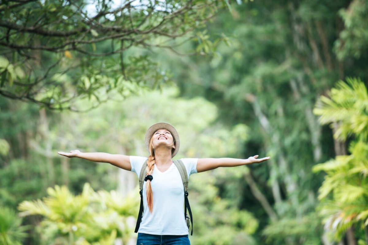 Young woman with arms outstretched, feeling joyful in a lush green forest.