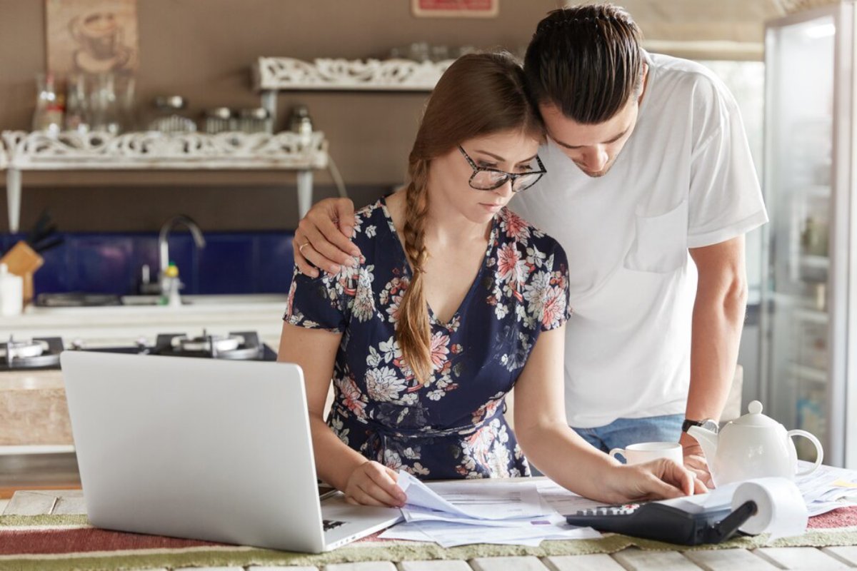 Young couple reviewing documents together in a kitchen with a laptop and tea set nearby.