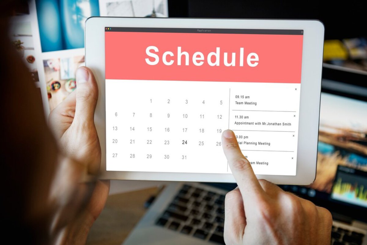 Person interacting with a digital calendar on a tablet screen, scheduling appointments and meetings.