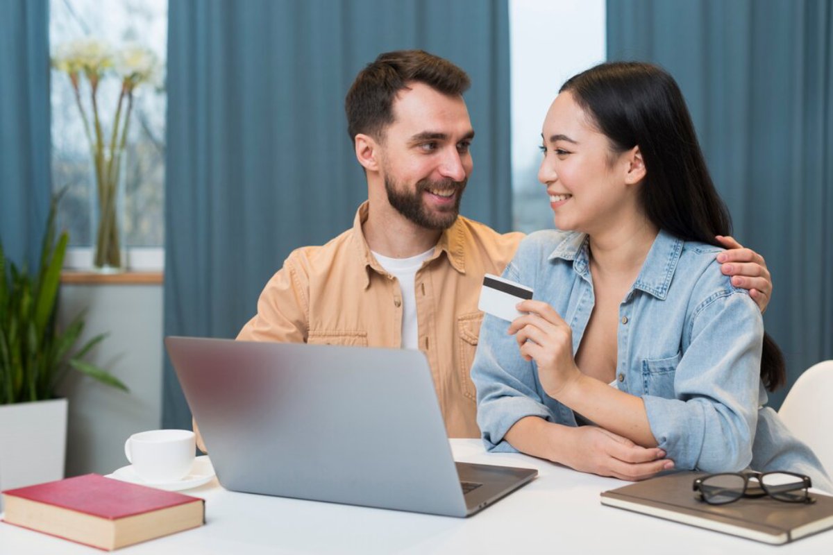A happy couple shopping online together with a laptop and a credit card in a bright room.