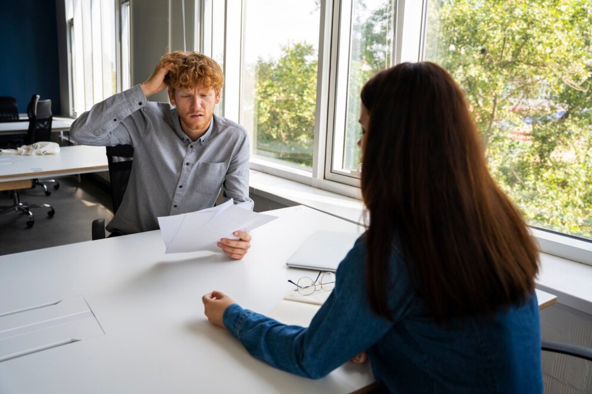 A young man looking stressed during a discussion with a woman in a modern office setting.