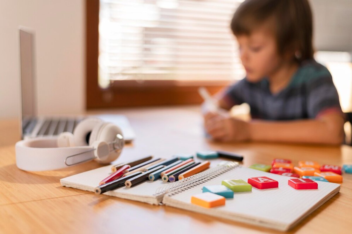 Young boy doing homework with colorful supplies and laptop on the table.