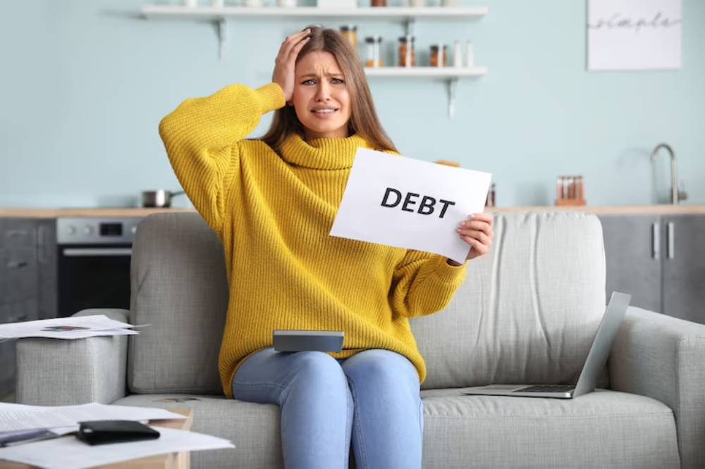 A woman in a yellow sweater sits on a couch, holding a sign that reads 
