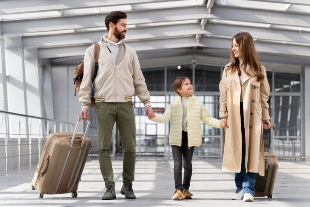 A family walks through an airport terminal, holding hands and carrying luggage.