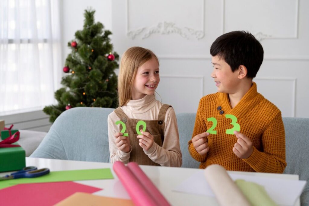 Two children holding numbers "2023" and smiling, with a Christmas tree in the background.