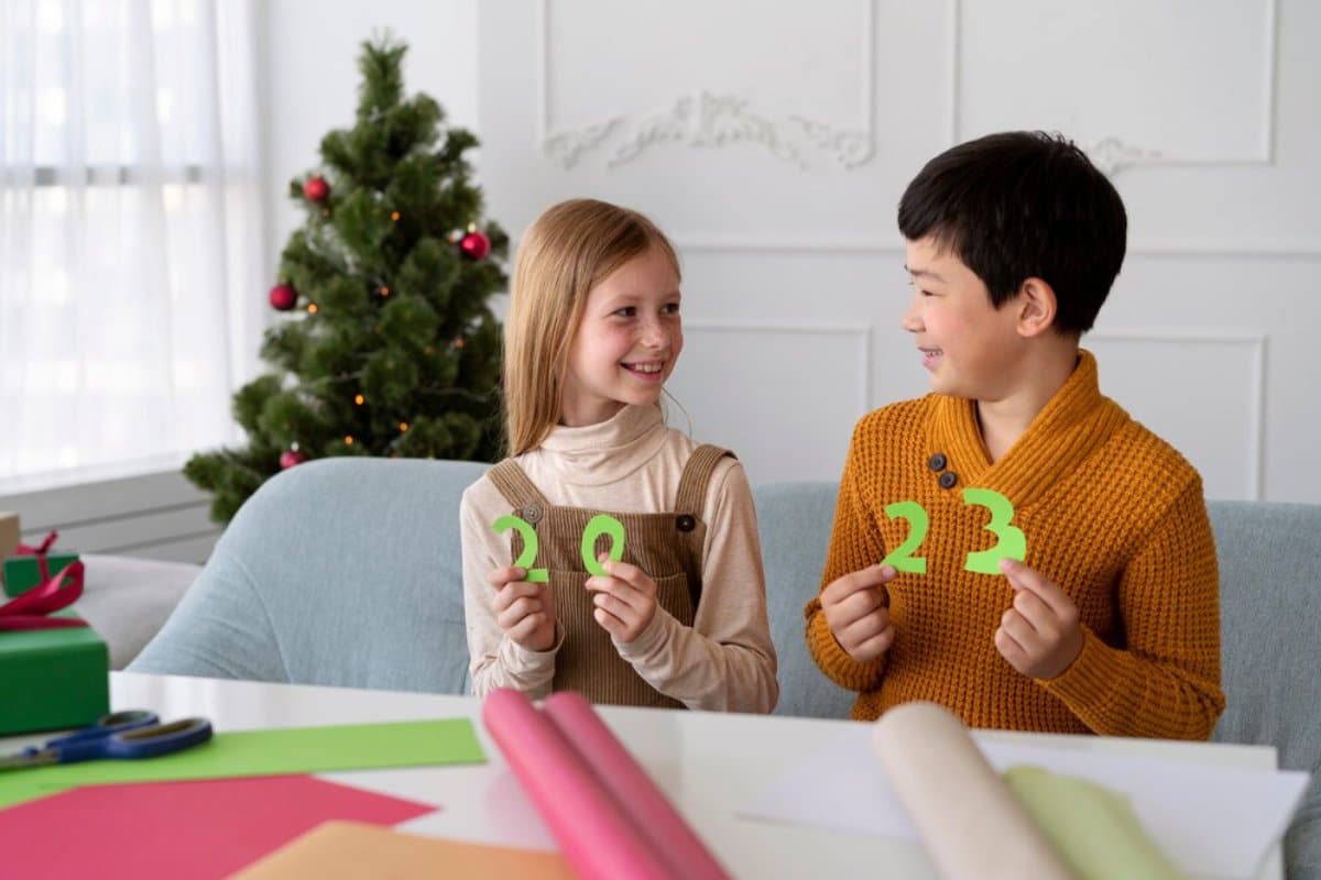 Two children holding numbers "2023" and smiling, with a Christmas tree in the background.