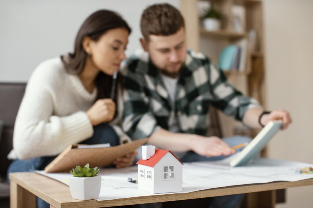 Young couple analyzing house plans with a small model home on the table in front of them.