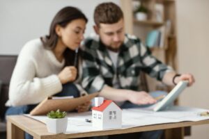 Young couple analyzing house plans with a small model home on the table in front of them.