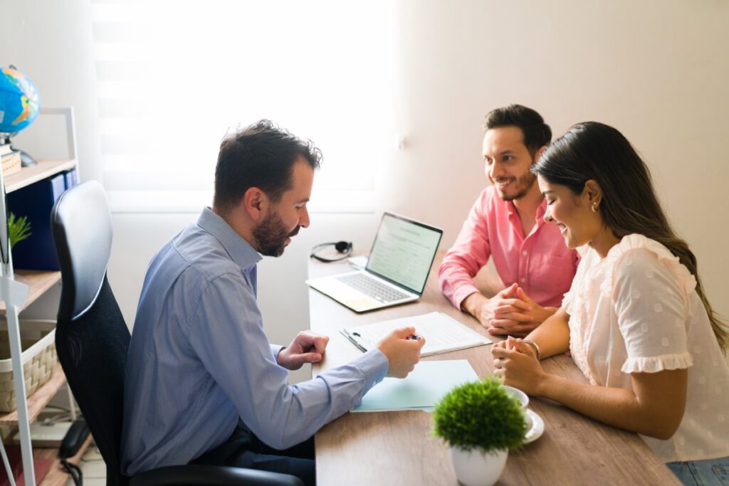 Three professionals discussing over documents and a laptop in a bright office setting.