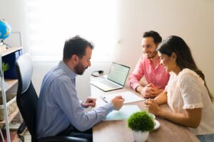 Three professionals discussing over documents and a laptop in a bright office setting.