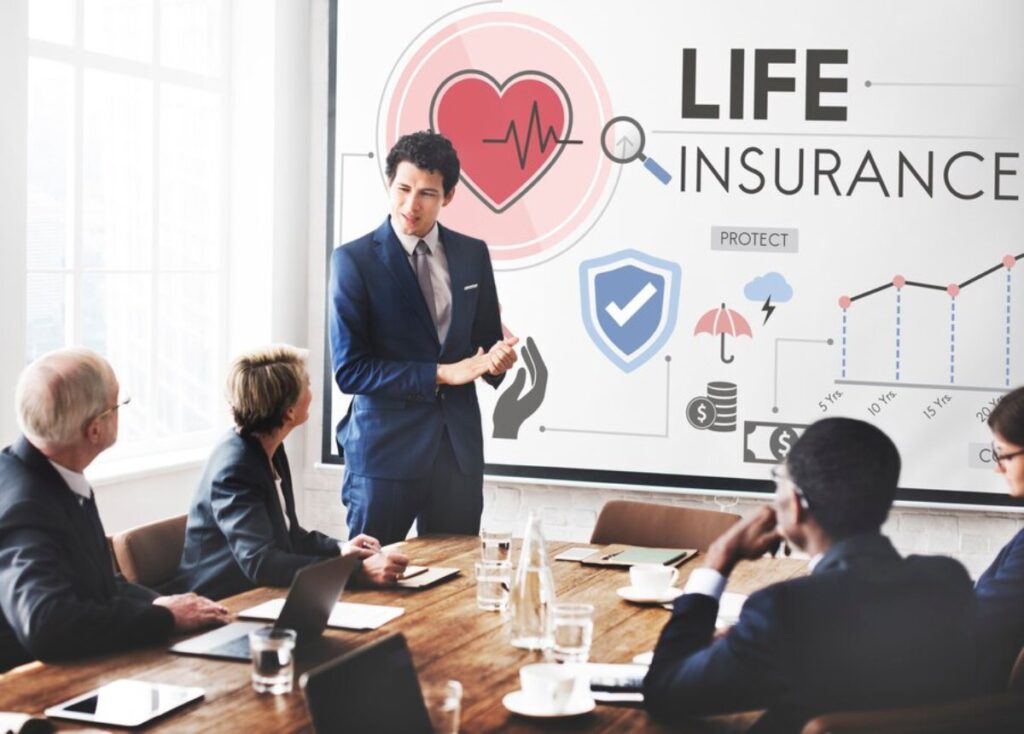 A man in a business suit presents life insurance concepts to colleagues in a meeting room with graphical display.