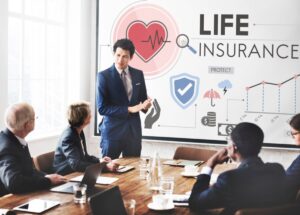 A man in a business suit presents life insurance concepts to colleagues in a meeting room with graphical display.