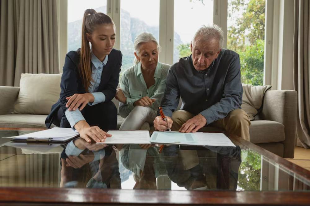 A family of three persons sitting around a coffee table, reviewing documents and signing paperwork, in a well-lit living room.
