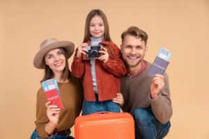 A family of three poses with passports and travel tickets, standing beside a bright orange suitcase against a pastel background.